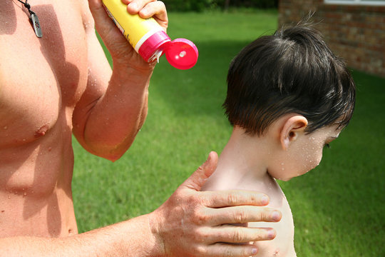 Boy Has Father Apply Sunscreen To Shoulders