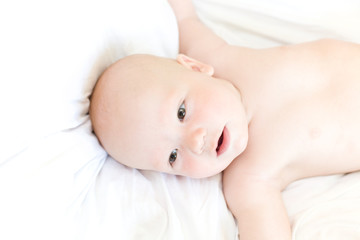 Funny little baby on white bed. View from above