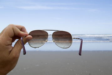 Fototapeta na wymiar Handhold Sunglasses in front of a beach.