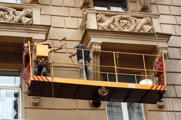 Two workers restoring old city building by tool
