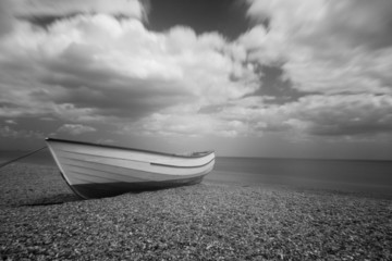 Open boat on a shingle beach in Suffolk UK. Mono Infrared image. - obrazy, fototapety, plakaty