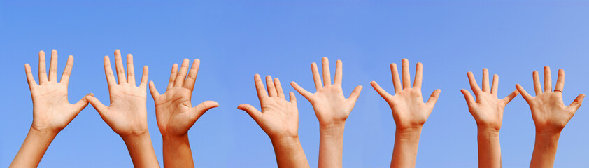Row of hands with open palms on blue sky background
