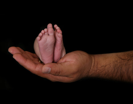 Father holding his newborn infant's feet on black