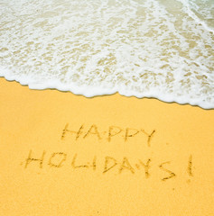 happy holidays written in the sandy beach