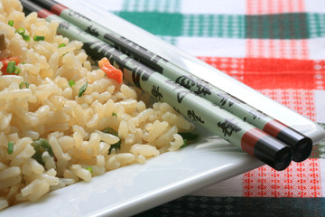 A plate of oriental fried rice with vegetables and chopsticks
