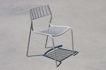 Lone gray metal chair with shadow on concrete