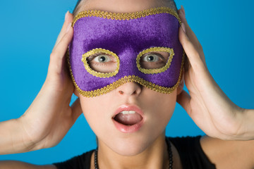 Young beautiful model in violet carnival mask. She's surprised