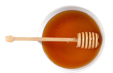 A bowl of amber honey with a honey wand isolated on white