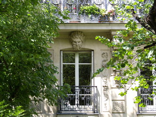 Fenêtre avec tête d'homme sculptée derrière arbres au soleil