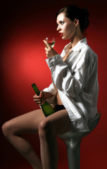 a woman is sitting in white men shirt with bottle.of white wine