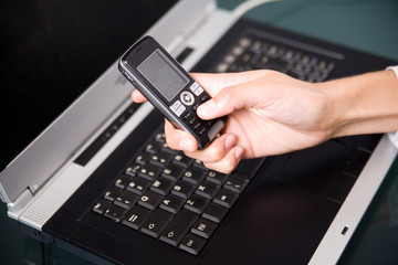 woman holding cell phone over the notebook's keyboard