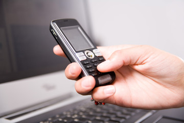 woman holding cell phone over the notebook's keyboard