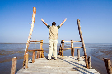 Man with his arms wide open on a dock