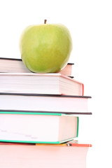 stack of books and green apple on desk - isolated on white