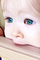 Little Baby biting on crib, taken closeup with green eyes