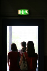 Three girls exit the building on exit door. Exit symbol