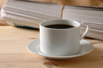 A newspaper rolled up behind a cup of coffee