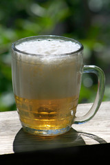 Mug of beer with foam on a wooden board.