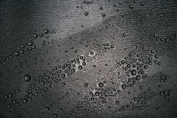 Small drops of water on a dark teflon surface.