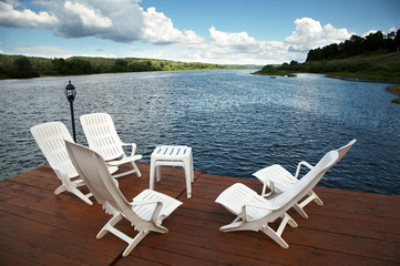 Five white armchairs and table on coast of a reservoir