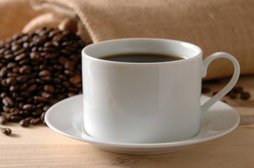 Coffee spills out of a burlap bag behind a fresh cup
