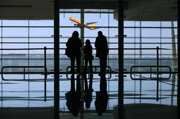 family looking to a airplane through the window in the airport