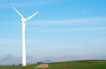 Wind powered electricity generator standing against blue sky