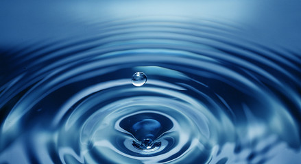 single water drop about to splash onto water's blue surface below