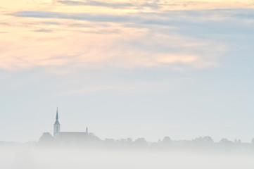 Fog church and trees with colorful sky. Early in the morning.