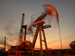 Silhouette of swinging oil pump in evening sky