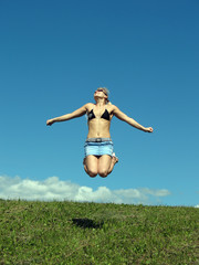 Jumping girl on the grass and blue sky.