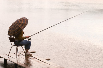 The woman fishes on lake under a rain