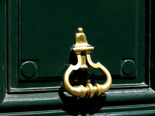 Poignée de porte en cuivre doré sur porte verte laquée.