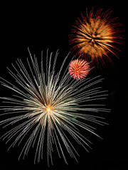 Three fireworks bursts in red-gold, pink, and white