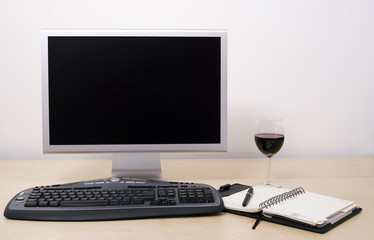 Computer in office with calendar, pen and glass of red wine. 