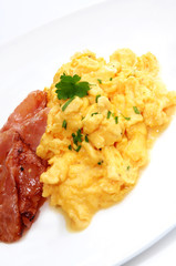 Breakfast of creamy scrambled eggs and bacon.