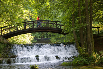 young couple crossing over wooden bridge and small waterfall