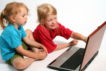 Two little girls playing on laptop on a white background