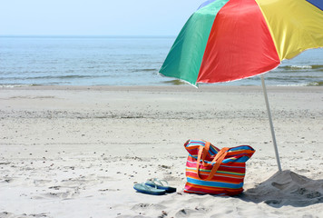 Beach bag,flipflop and umbrella against blue sea and sand .