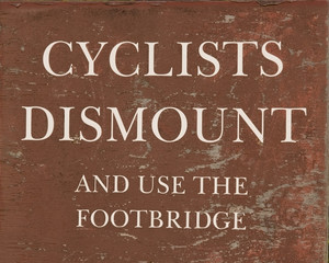 A weathered, brown "cyclists dismount" sign