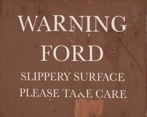 A weathered, brown "warning - ford" sign