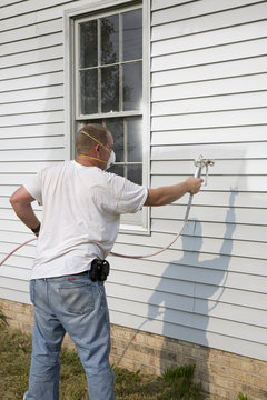 Contractor spray painting exterior of house
