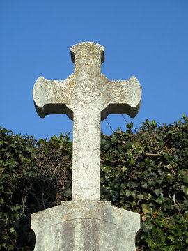 Old stone Celtic cross tops a cemetery headstone.