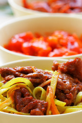 Chinese noodles and fried beef within bowl close-up