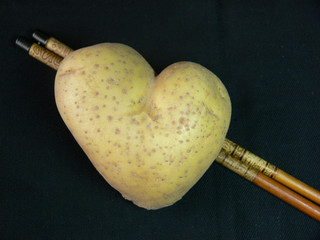 Herzkartoffel vor schwarzem Hintergrund mit Stäbchen