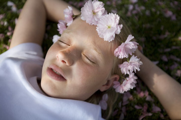 Obraz na płótnie Canvas girl with cherry blossom in her hair resting in the grass