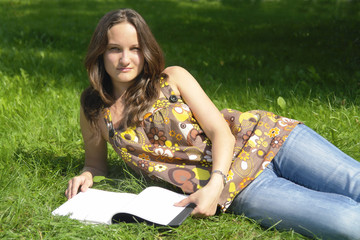 young brunette girl lying on the grass with an open book