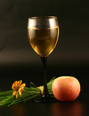 Glass of wine, apple and grass on a black background.