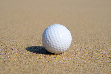 A golf ball in the sand with shallow focus.