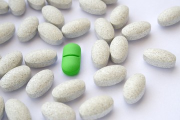 Fototapeta na wymiar Zielona pigułka wśród szarych tabletkach